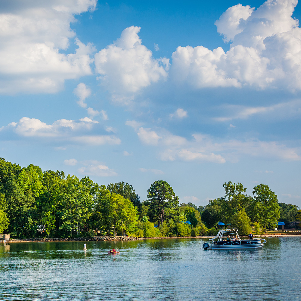 The image shows a serene lake scene with boats on the water, surrounded by trees and a clear blue sky.